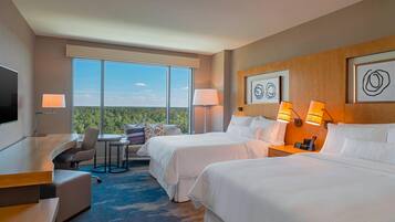 A hotel room with two beds, a desk, a chair, and a view of the outdoors.