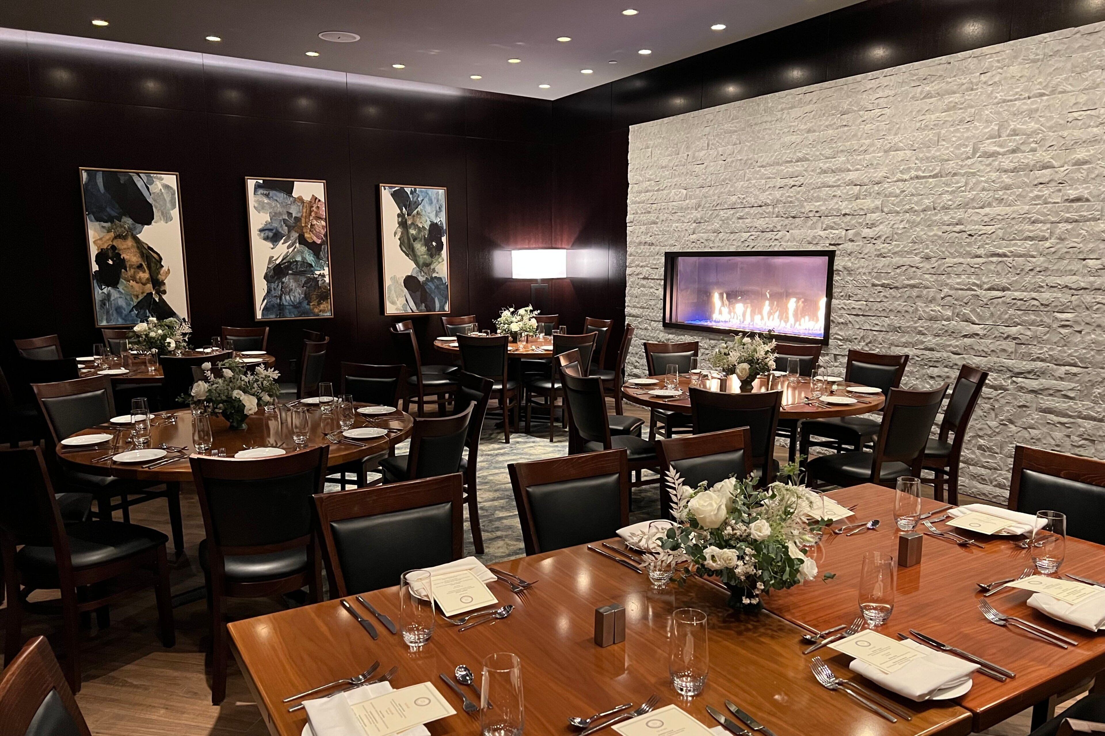 A restaurant with multiple dining tables, chairs, and a television mounted on a stone wall.