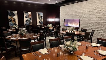 A restaurant with multiple dining tables, chairs, and a television mounted on a stone wall.