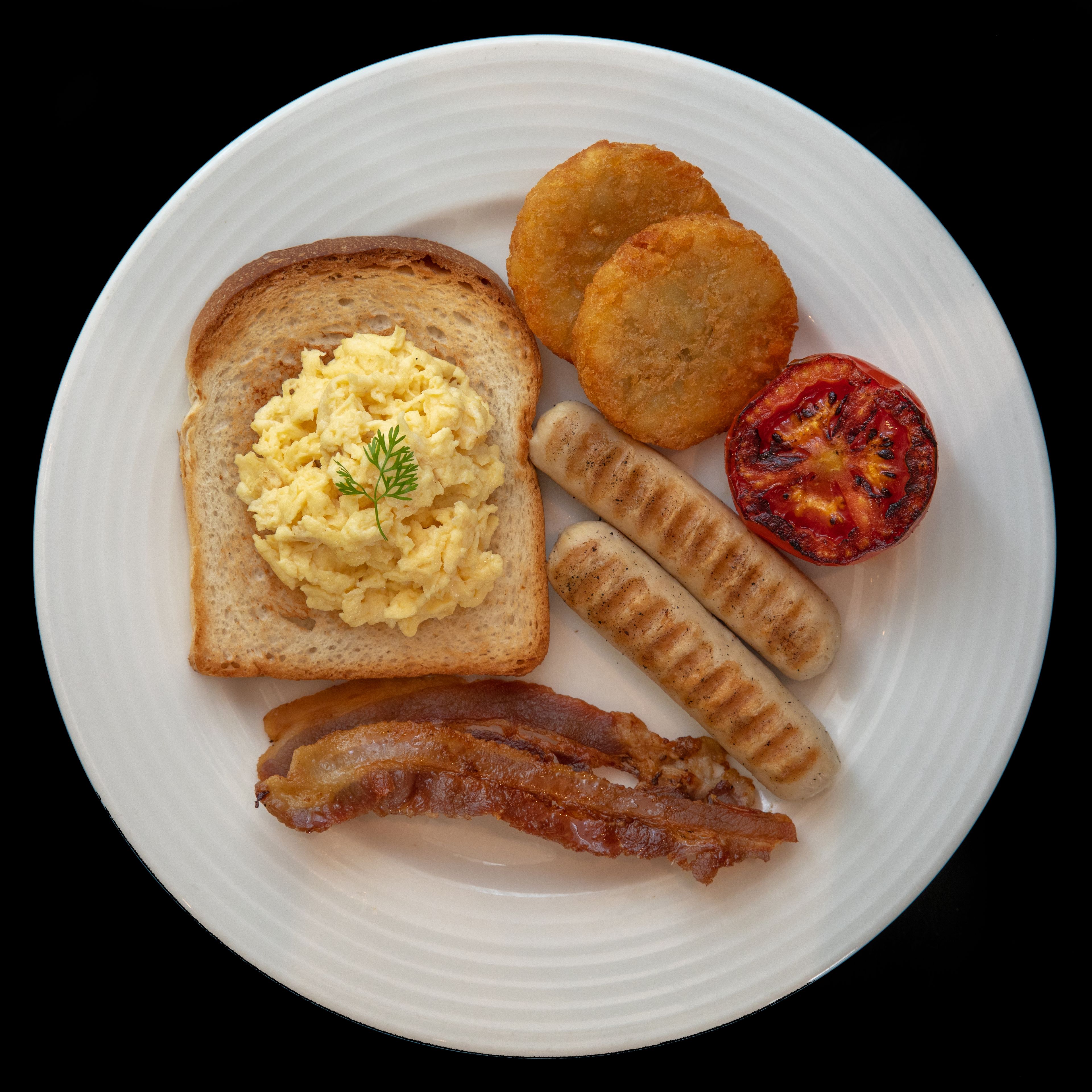 A plate with scrambled eggs, toast, sausages, a grilled tomato, and bacon.