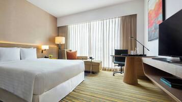 Una habitación de hotel con una cama grande, un escritorio, una silla, un televisor y una ventana con cortinas.
