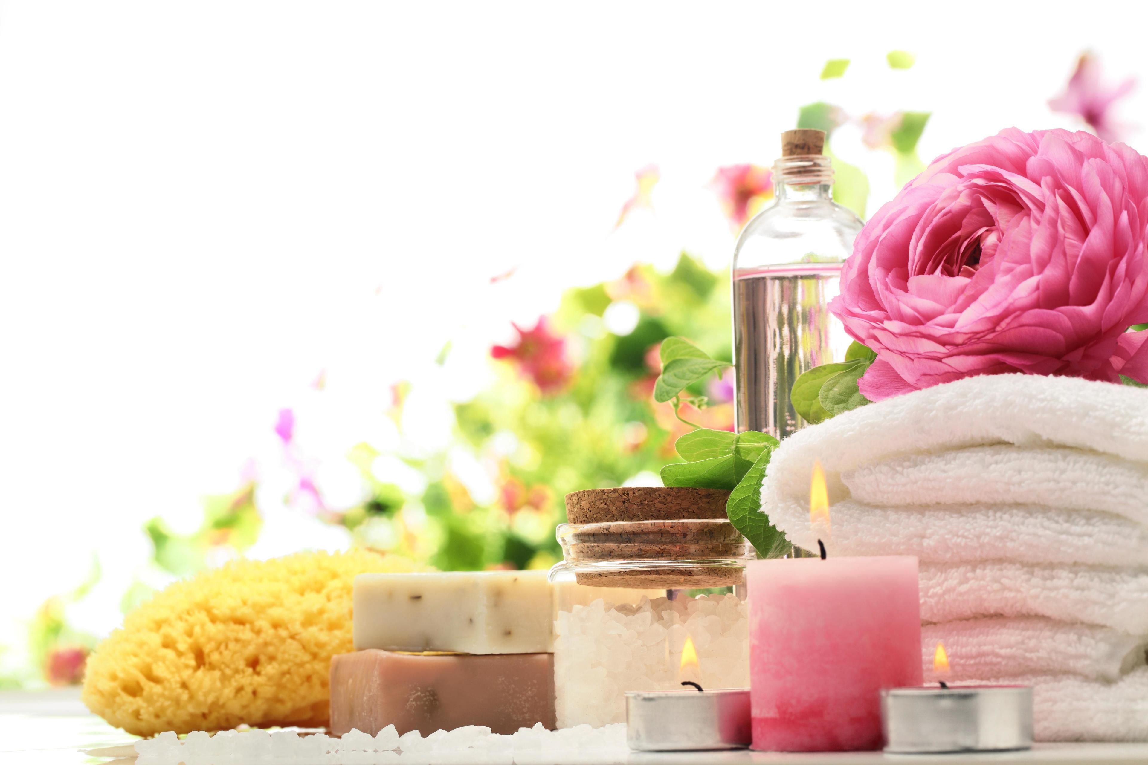 A spa setting with various bath products, candles, and a pink flower.