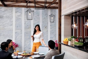 Un espace repas agrémenté d’un mur en marbre, de luminaires suspendus et d’un bar où sont exposées des bouteilles et des fruits.