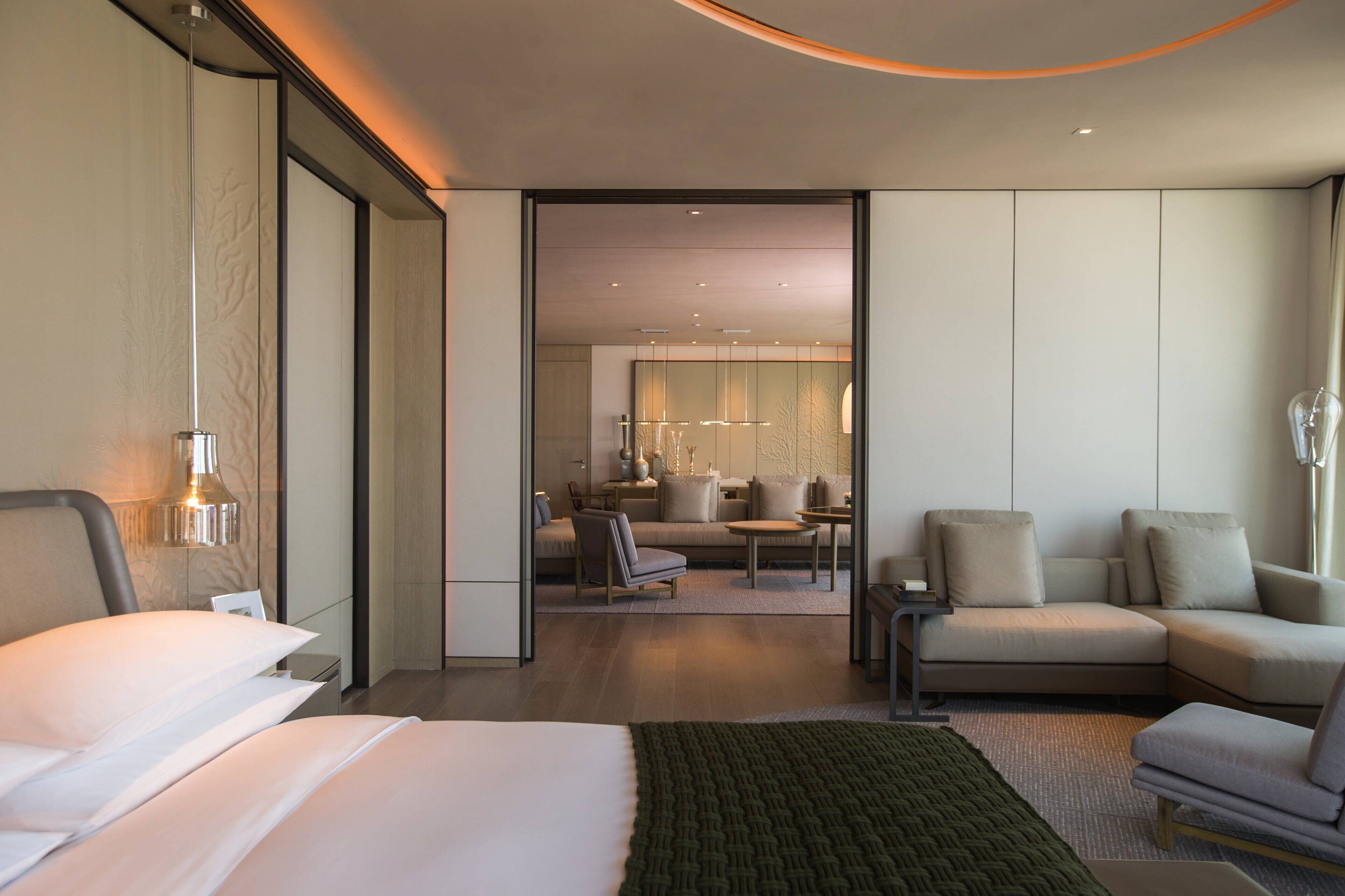 A modern hotel room with a large bed, a sitting area with a sofa and chairs, and a dining table.