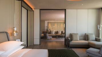 A modern hotel room with a large bed, a sitting area with a sofa and chairs, and a dining table.