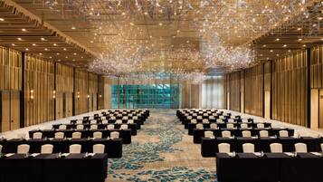 A conference room with rows of tables and chairs, a patterned carpet, and a ceiling with hanging lights.