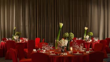 Ein formeller Speisesaal mit roten Stühlen und Tischen, gedeckt für eine Mahlzeit, mit floralen Tischdekorationen und Kerzen.