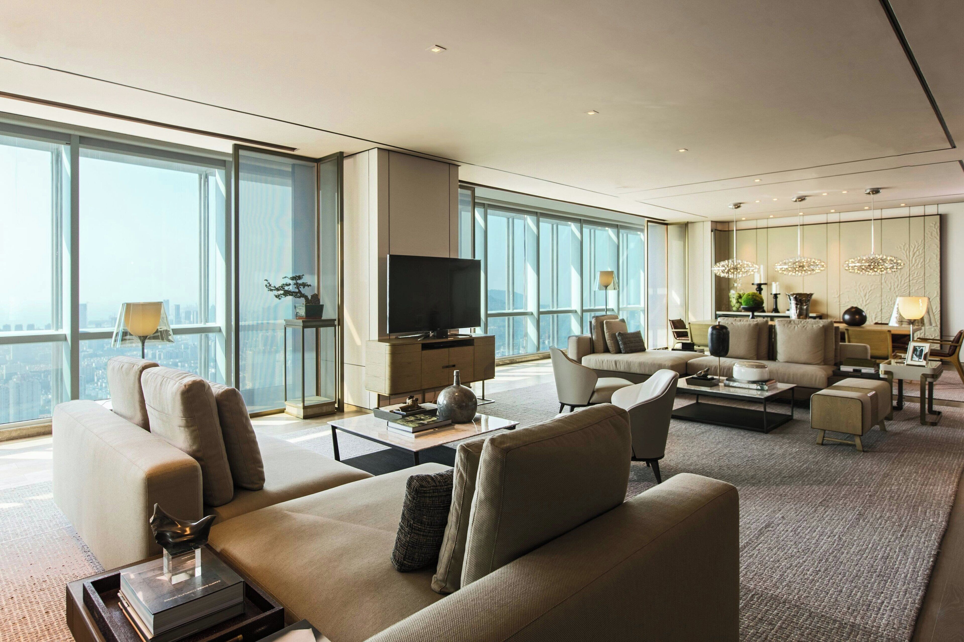 A spacious living room with a large flat-screen TV, comfortable seating, and large windows offering a city view.