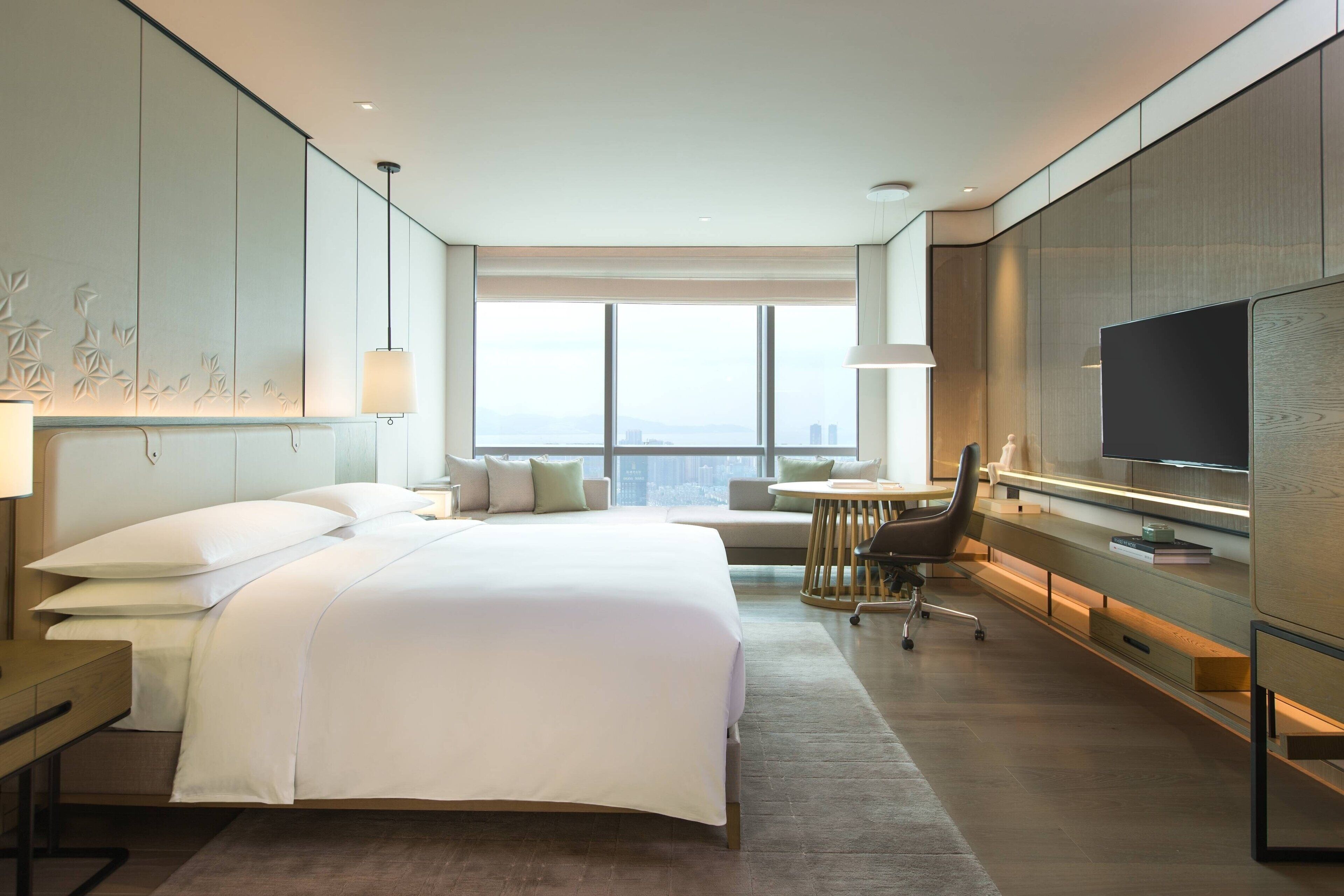 Une chambre d’hôtel moderne dotée d’un grand lit, d’un bureau, d’une chaise, d’une télévision et offrant une vue sur la ville.