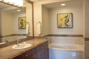 A modern bathroom with a marble sink, a large mirror, a bathtub, and two wall-mounted towels. - Broadway Plaza, Trademark Collection by Wyndham (Rochester)