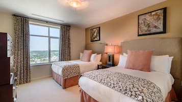 A hotel room with two beds, a large window, a ceiling fan, and artwork on the walls.