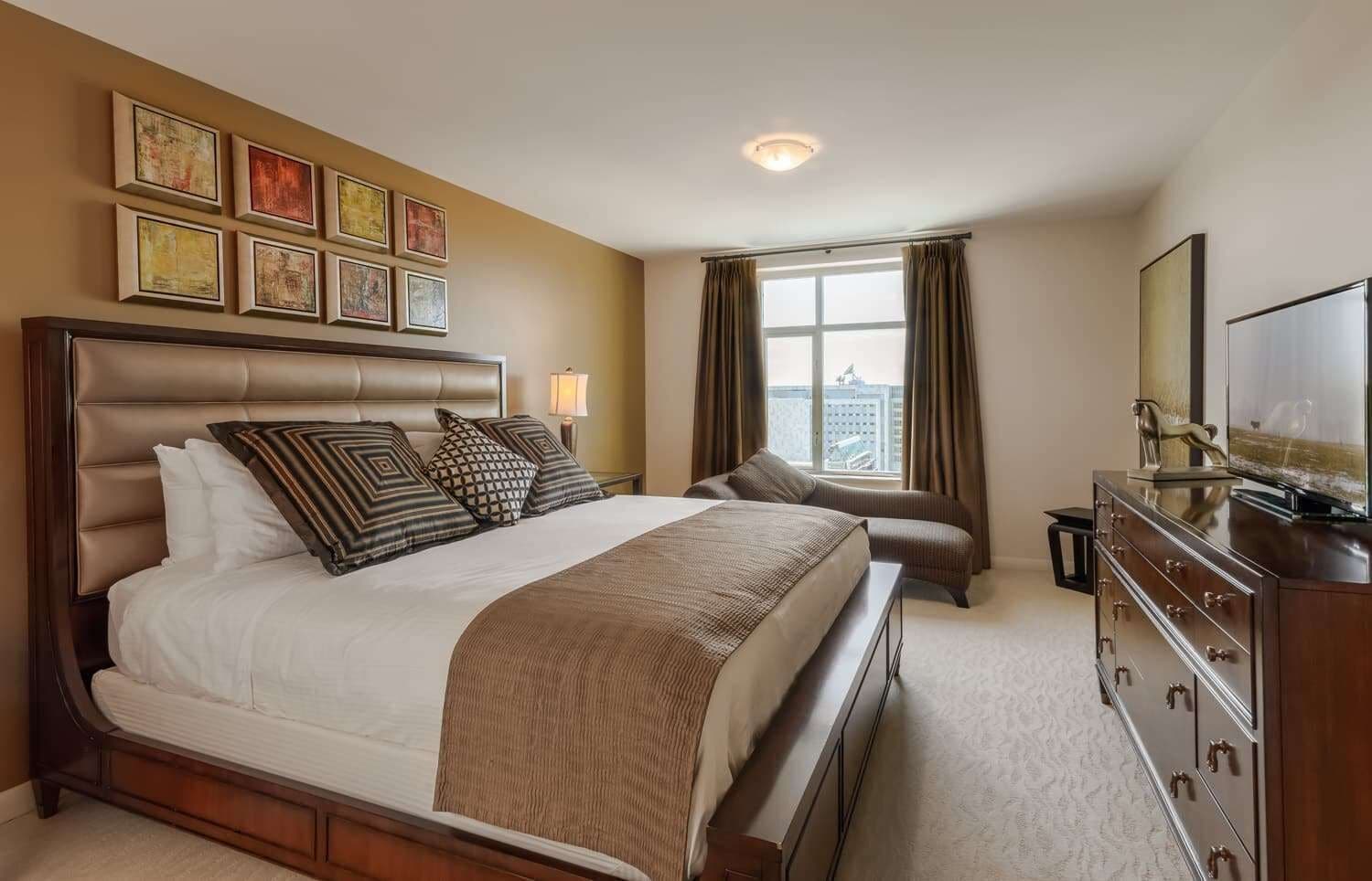 Una habitación de hotel con una cama grande, un televisor, un aparador y una ventana con cortinas.