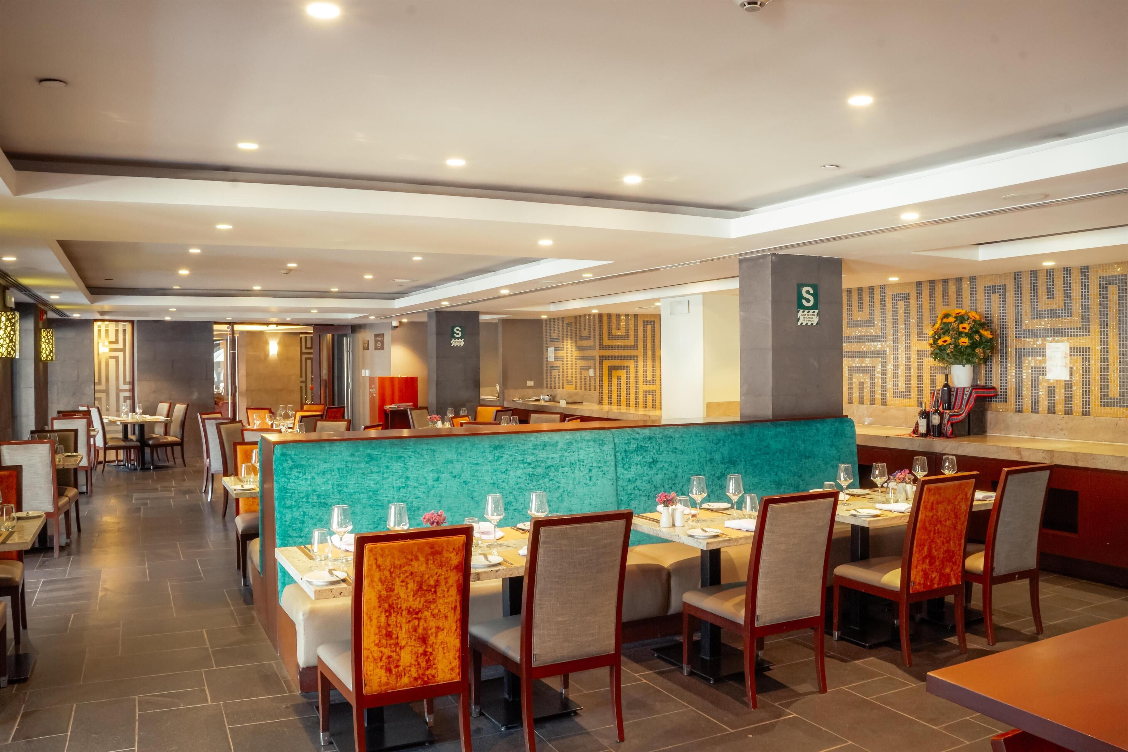 A modern restaurant with a teal-colored booth seating area, wooden chairs, and a bar counter.