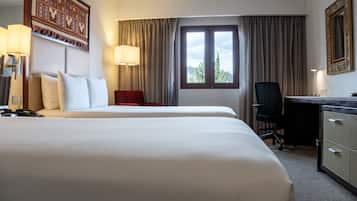 A hotel room with two beds, a desk, a chair, a lamp, and a window with curtains.