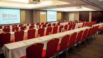 A conference room at Hilton Garden Inn Cusco - Peru with rows of red chairs and white tables, equipped with projectors and a large screen.