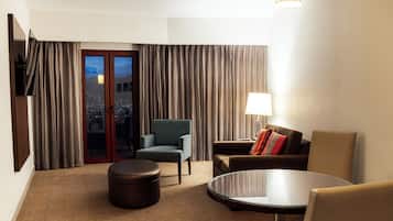 Habitación de hotel con zona de estar, una mesa redonda, sofá con lámpara y vistas a la ciudad a través de un ventanal.