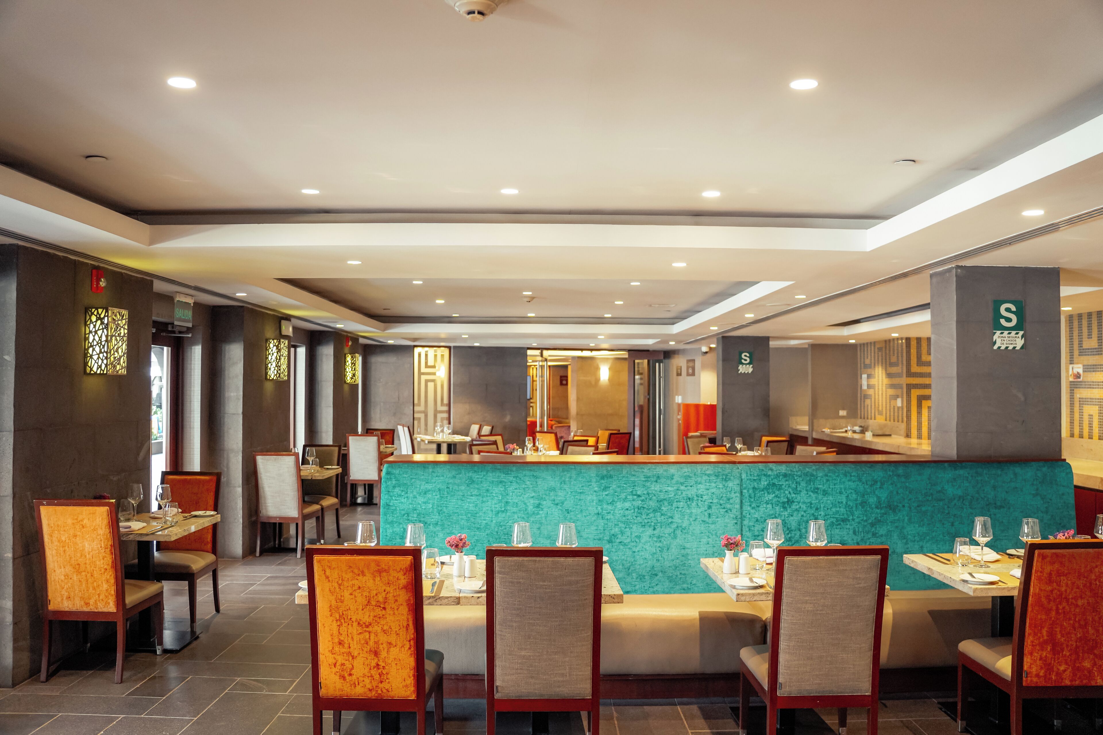 A modern restaurant with a teal-colored counter, wooden chairs, and a clean, well-lit interior.