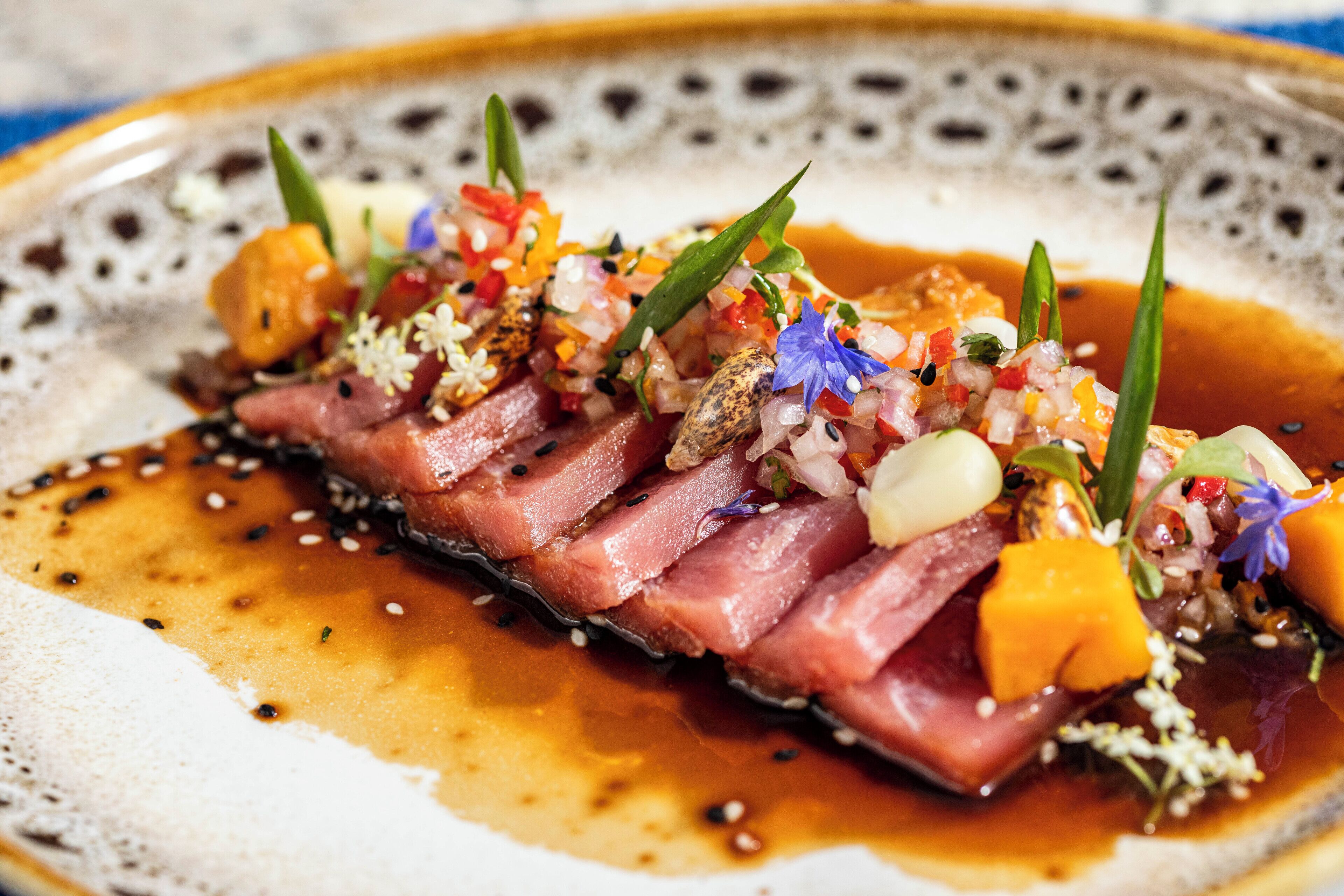 Um prato com carne fatiada finamente, legumes e molho sobre um disco decorativo.