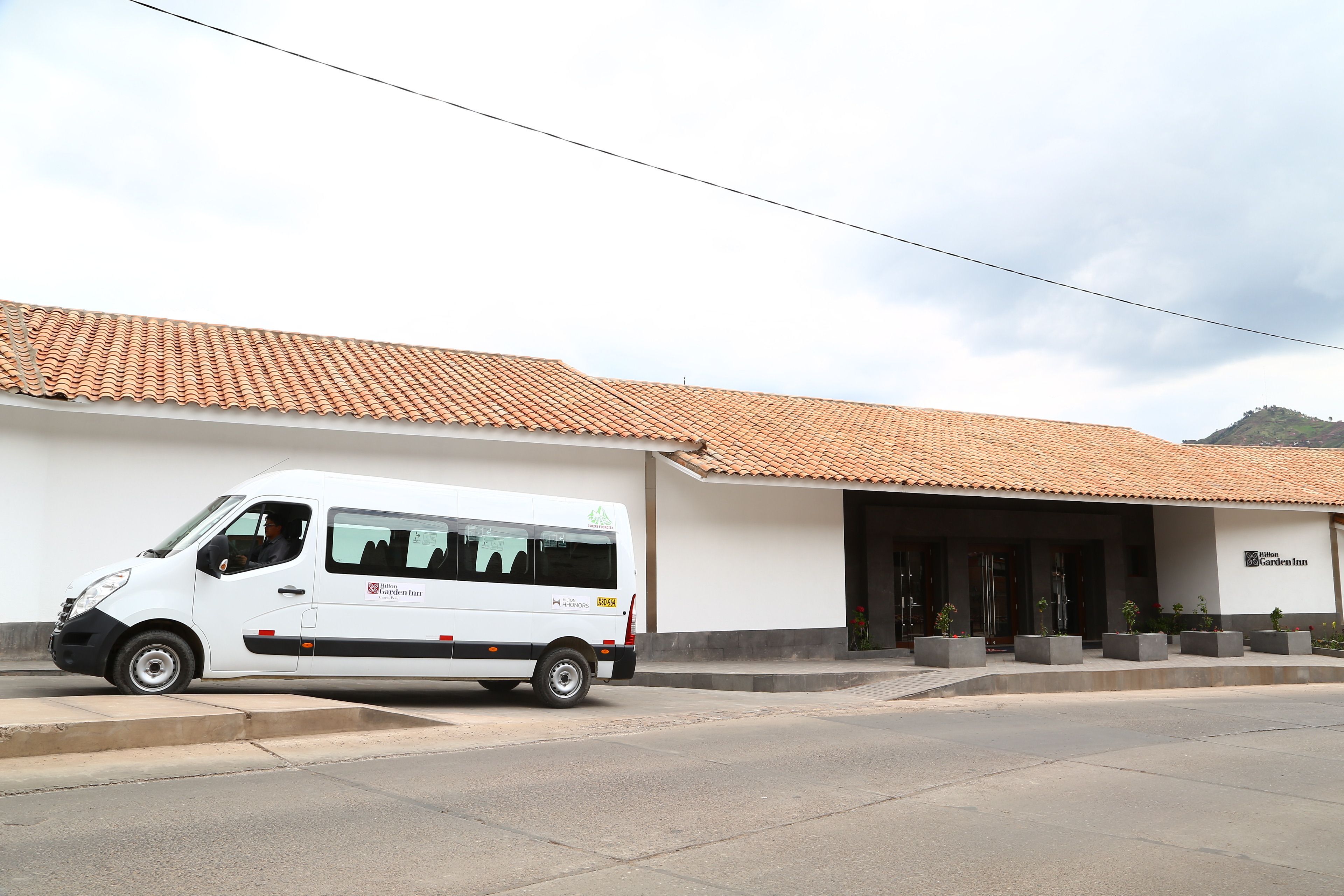 A white van parked in front of a building with a tiled roof and a sign reading "Hilton Garden Inn."