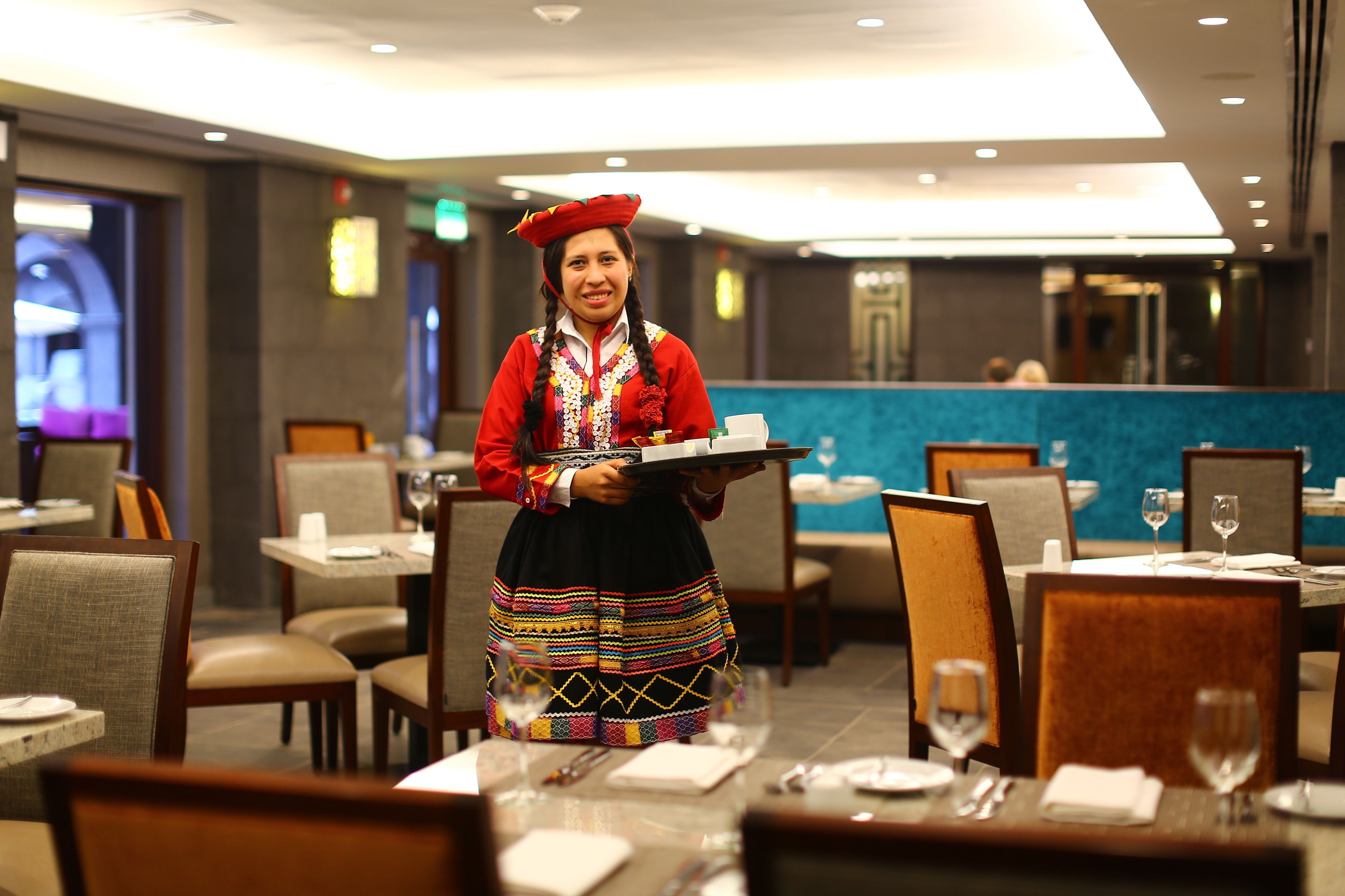 En hotelrestaurant med borde dækket til gæster, en tjener i traditionelt tøj, og et moderne interiør.