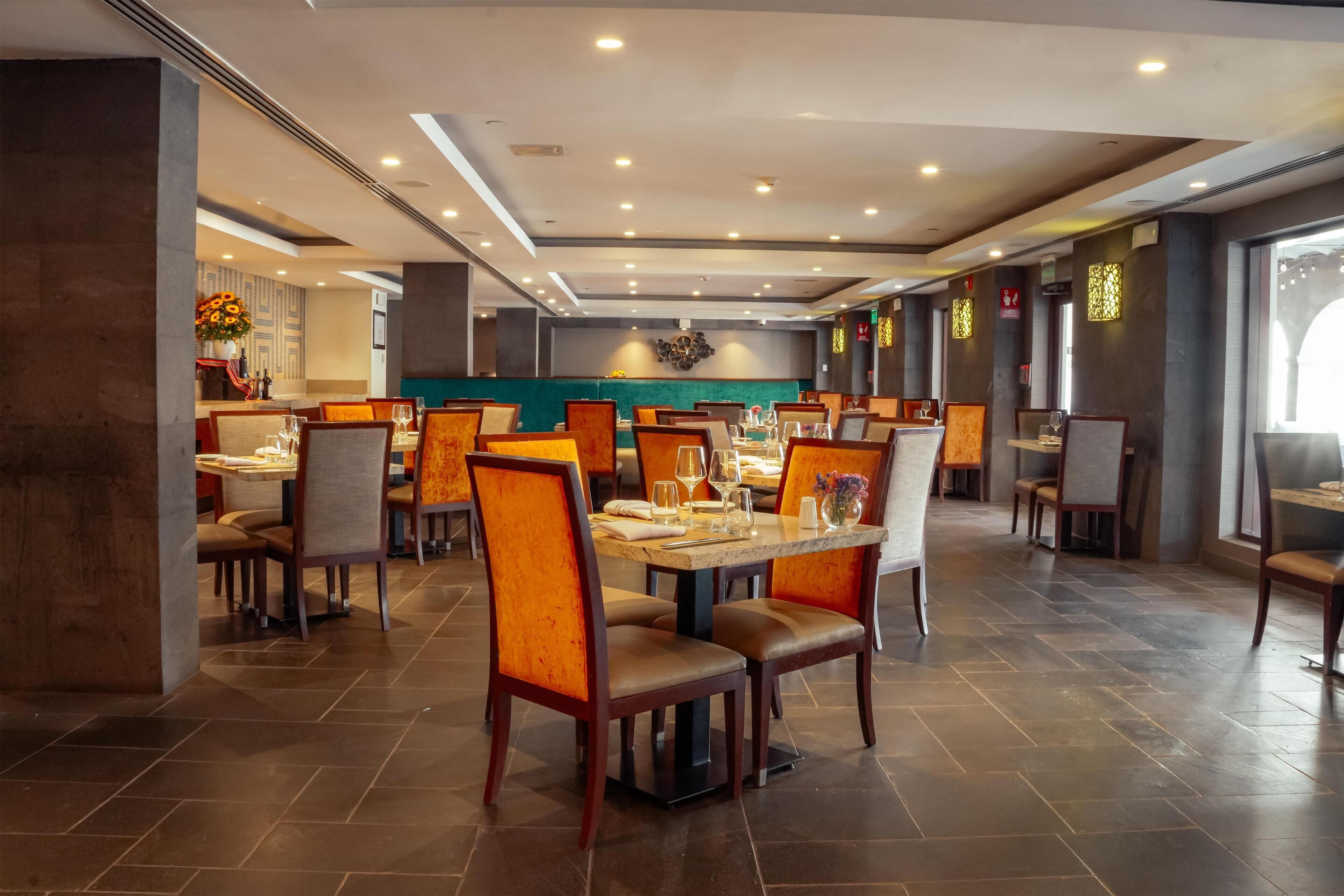 A spacious restaurant with multiple tables and chairs, a modern ceiling design, and a view of the kitchen area.