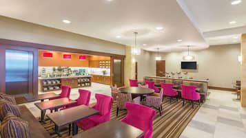 Un vestíbulo de hotel con zona de comedor, asientos y una cocina al fondo.