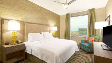 A hotel room with a large bed, two bedside lamps, a ceiling fan, a TV, and a window with curtains.