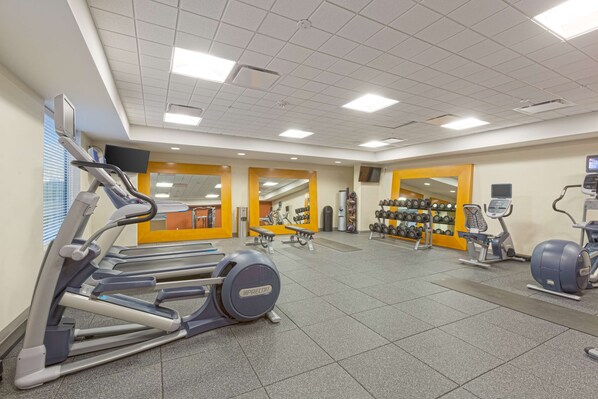 Un gimnasio con cintas de correr, elípticas y equipo de levantamiento de pesas.
