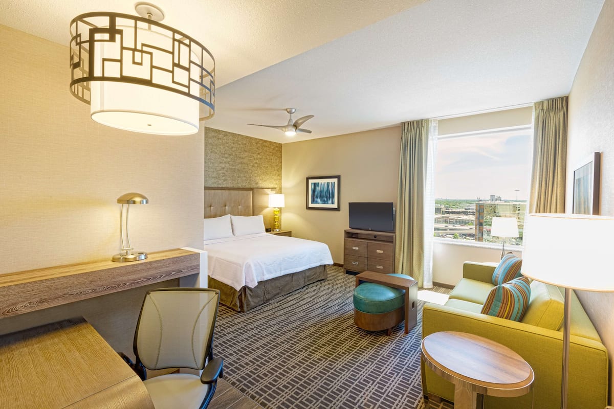 A hotel room with a bed, a desk, a chair, a sofa, a TV, and a window with a view.