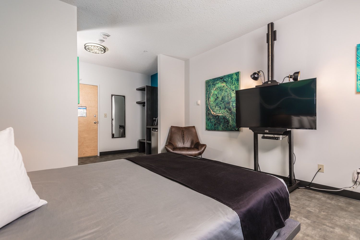 A hotel room with a bed, a chair, a TV, and artwork on the wall.
