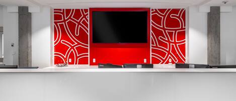 A modern reception desk with a large flat-screen TV, red patterned walls, and a minimalist design.