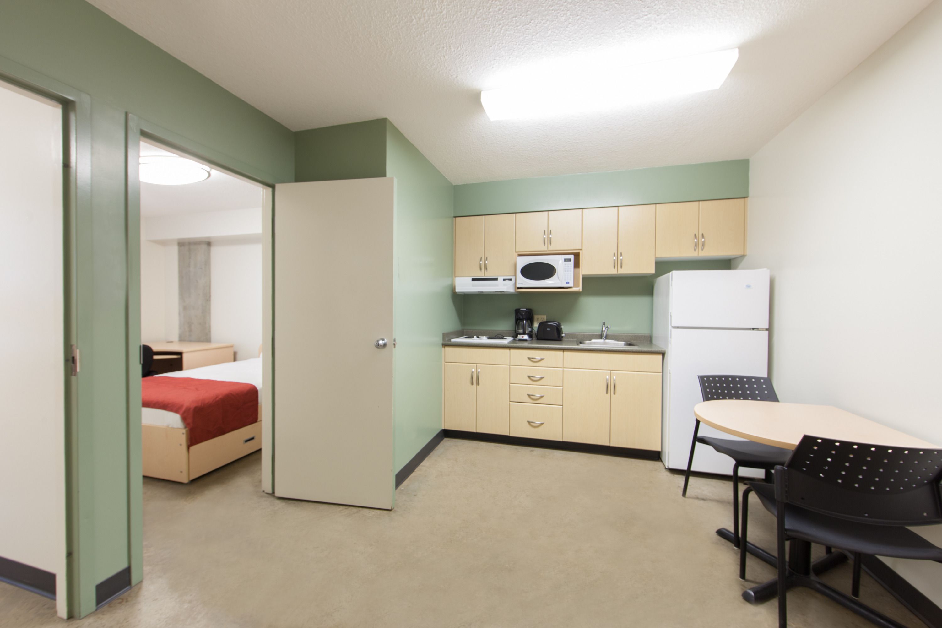 A compact kitchen with a microwave, coffee maker, and refrigerator. A small dining area with a table and chairs is adjacent to the kitchen.