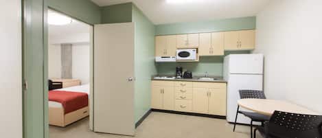 A compact kitchen with a microwave, coffee maker, and refrigerator. A small dining area with a table and chairs is adjacent to the kitchen.