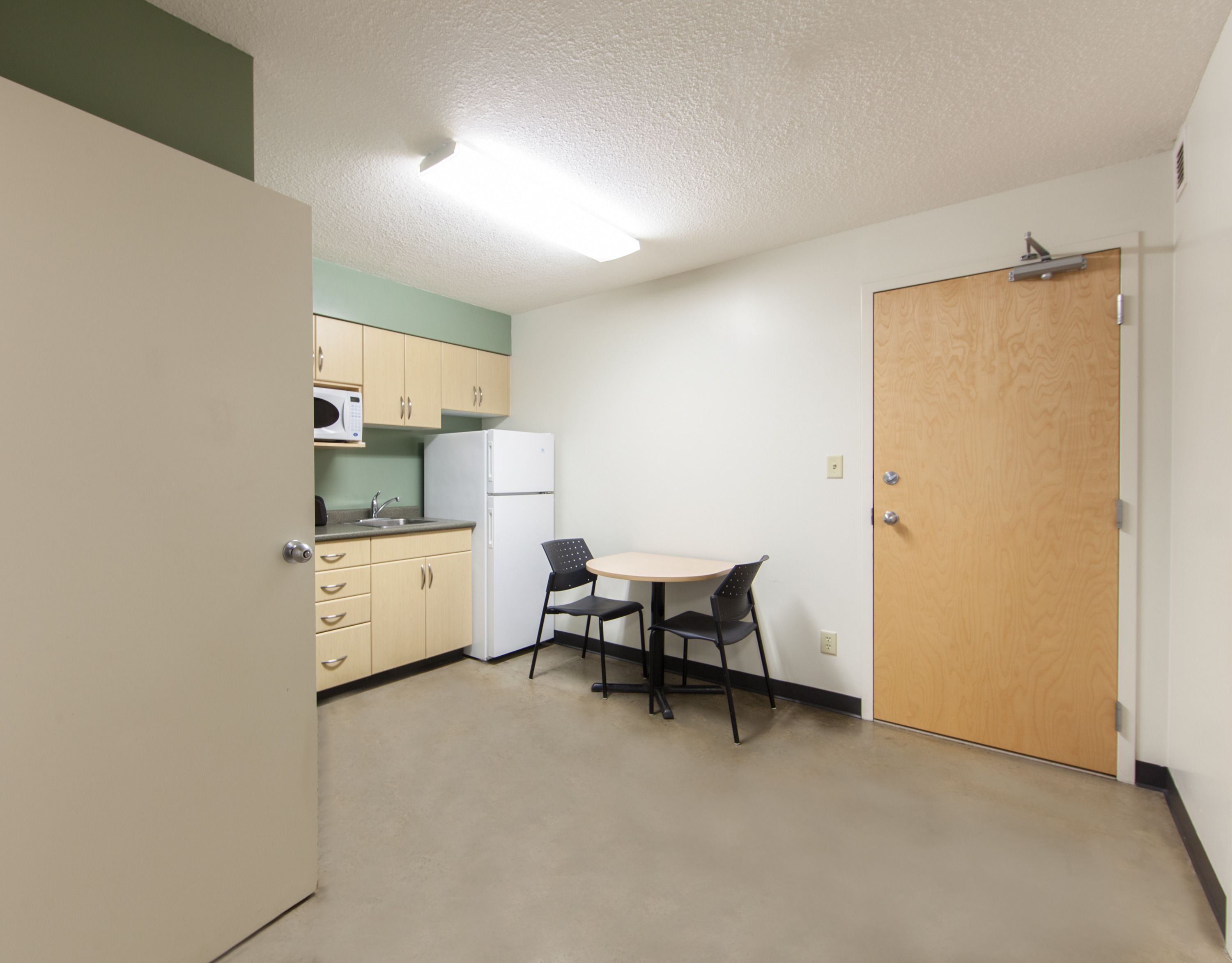 A compact kitchen with a microwave, refrigerator, and a small dining table with two chairs.