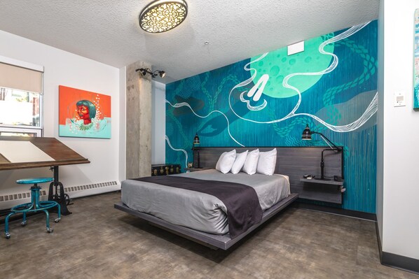 A modern bedroom with a large bed, a desk, and a vibrant mural on the wall.