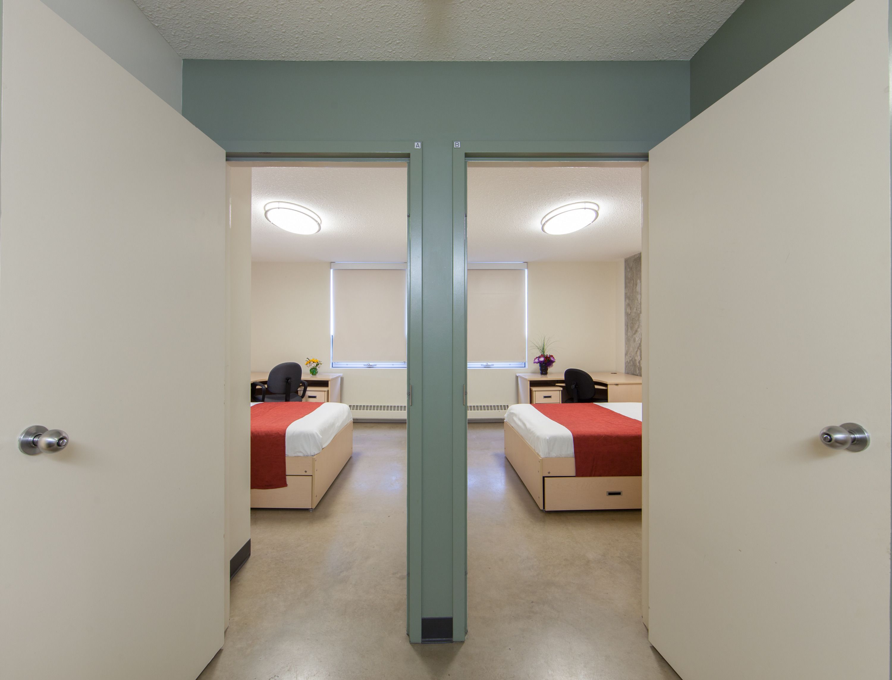 A hotel room with two beds, a desk, a chair, a window with blinds, and a mirror.
