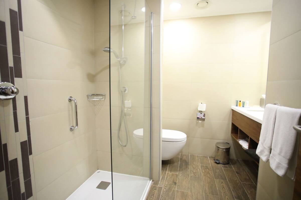A modern bathroom with a glass-enclosed shower, a white toilet, and a wooden vanity with a towel.