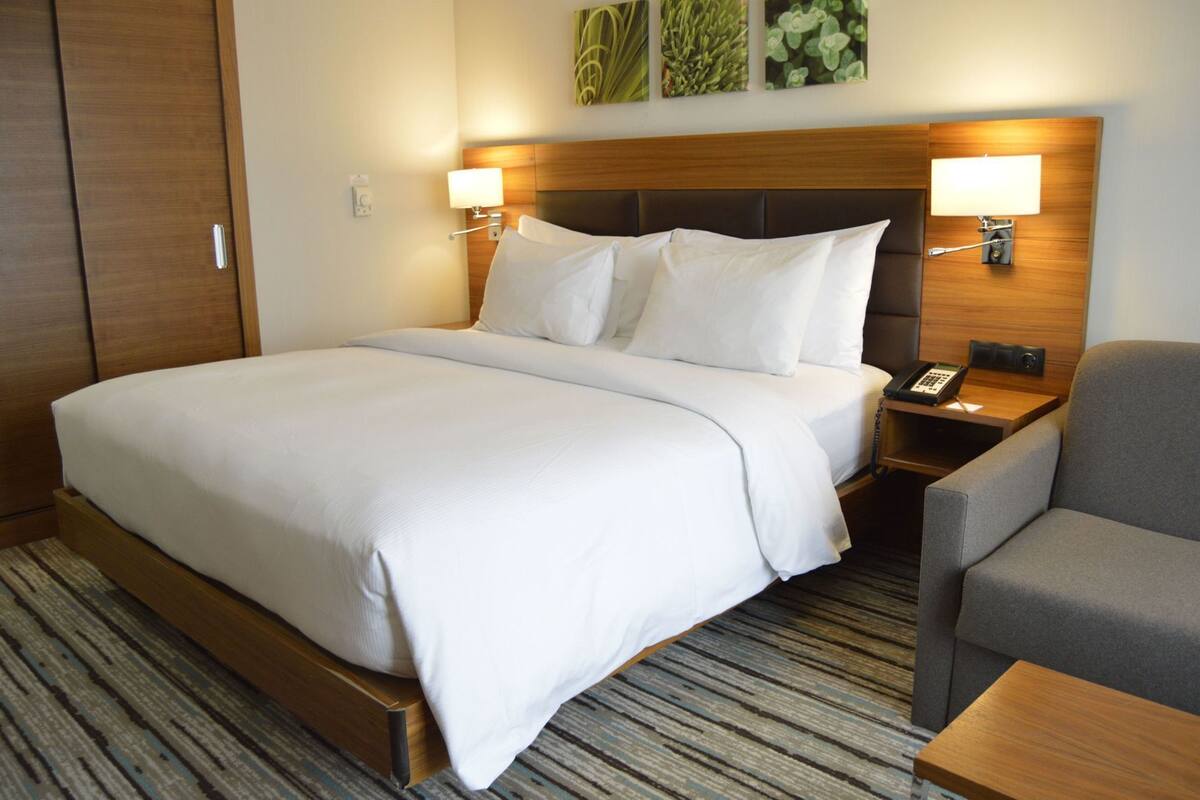 A hotel room with a large bed, two bedside tables, a chair, and a wooden headboard.