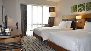 A hotel room with two beds, a desk with a coffee maker, a chair, and a large window with curtains. - Hilton Garden Inn Ankara Gimat (Ankara)