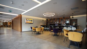 A modern restaurant with a bar area, wooden paneling, and yellow chairs. - Hilton Garden Inn Ankara Gimat (Ankara)