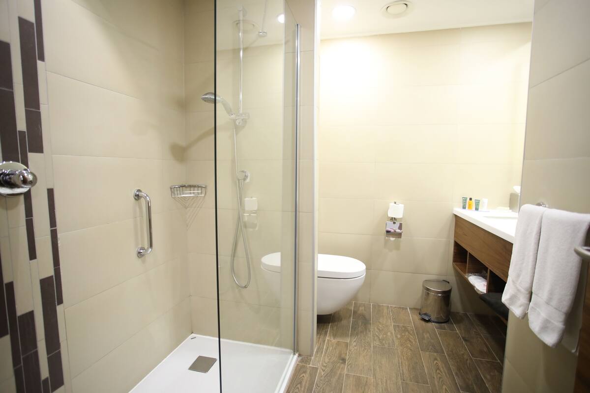 Une salle de bain moderne avec une douche à parois de verre, des toilettes blanches et un meuble-lavabo en bois, avec une serviette accrochée au mur.