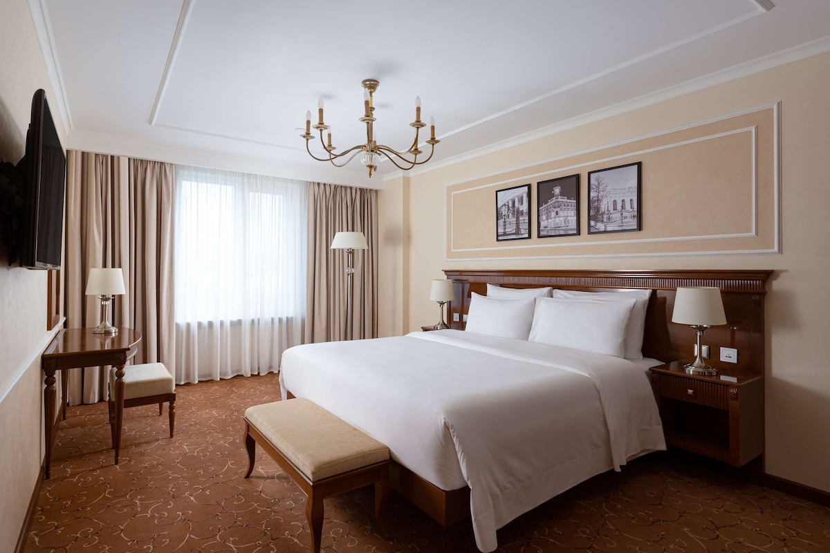 Una habitación de hotel con una cama grande, un escritorio, una silla, un televisor y una araña.