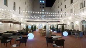 An outdoor patio area with tables and chairs, string lights, and umbrellas.
