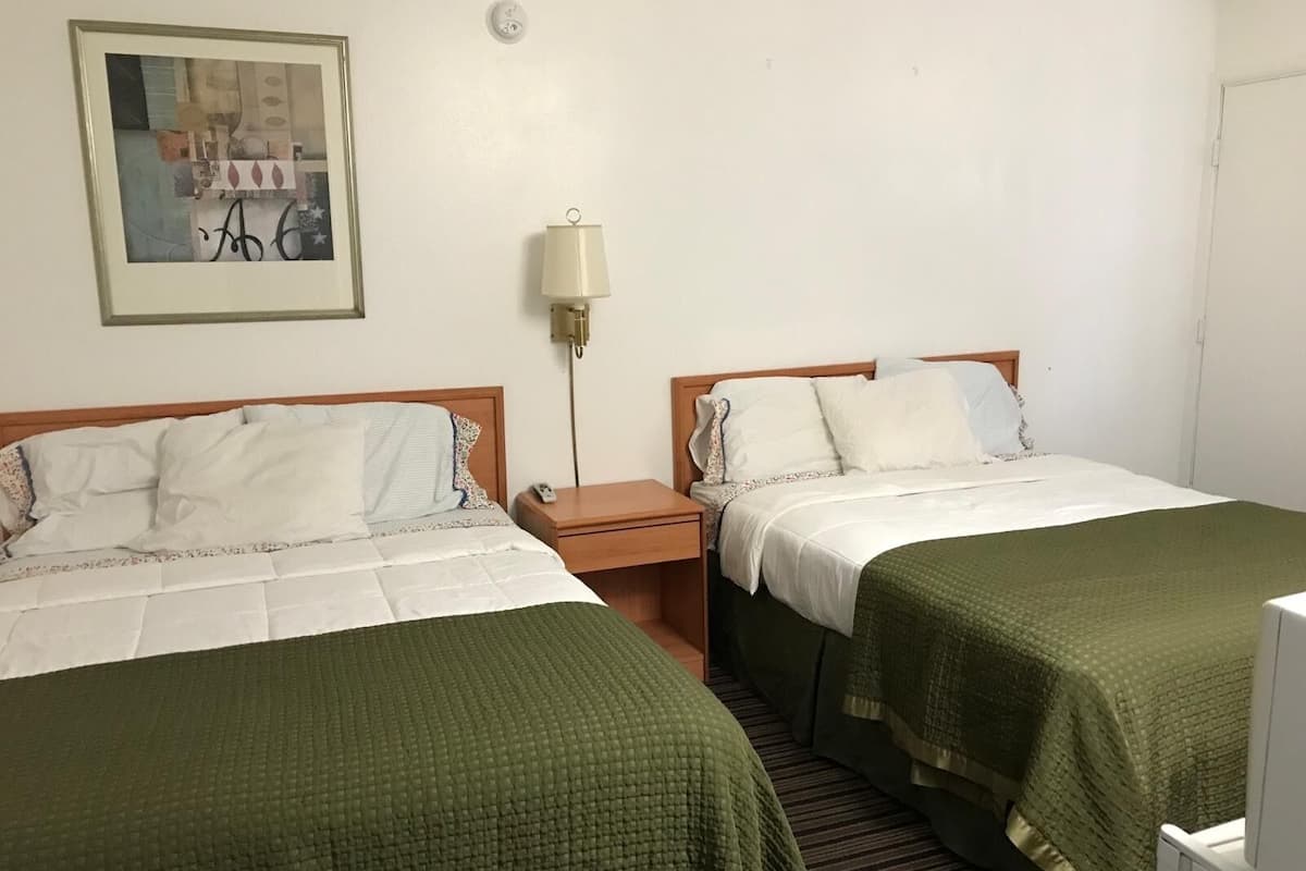 A hotel room with two single beds, a nightstand, a lamp, and a framed picture on the wall.