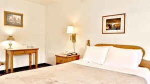 A hotel room with a bed, bedside table, lamp, and two framed pictures on the wall. - Blue Mountain Hotel (Dayton)