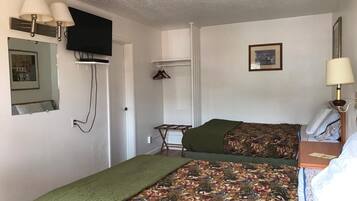 Una habitación con dos camas, un televisor montado en la pared, un perchero y un cuadro enmarcado.