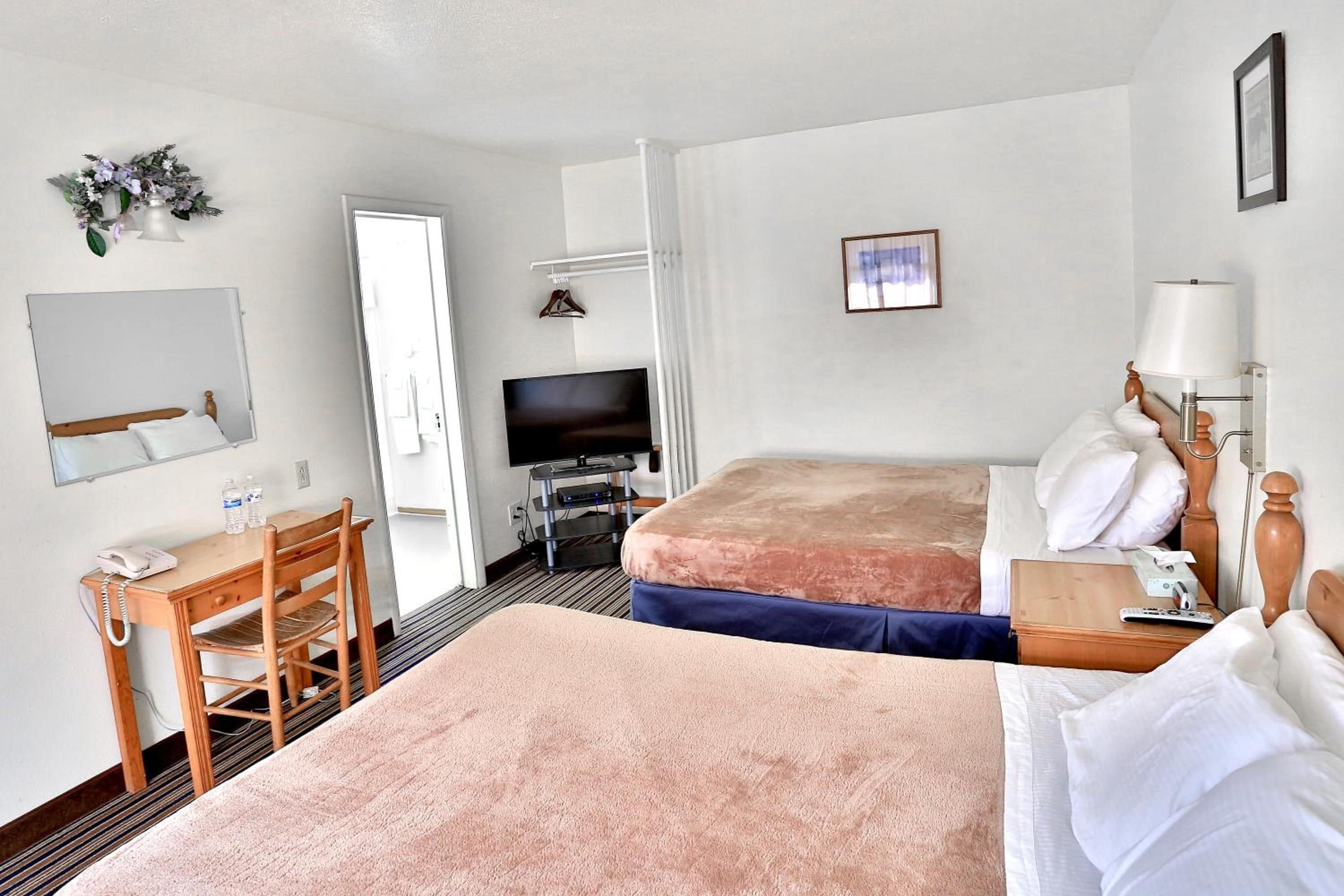 Una habitación de hotel con dos camas, un escritorio con teléfono, televisor y espejo.