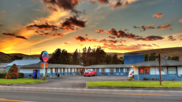 A motel with a large neon sign, a parking lot, and a red car parked in front. - Blue Mountain Hotel (Dayton)