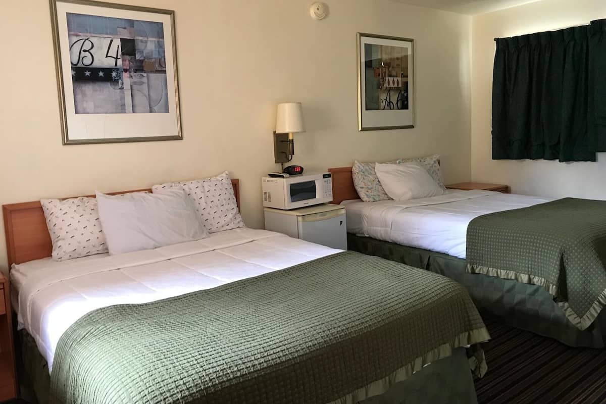 A hotel room with two beds, a microwave, a clock, and two framed pictures on the wall.
