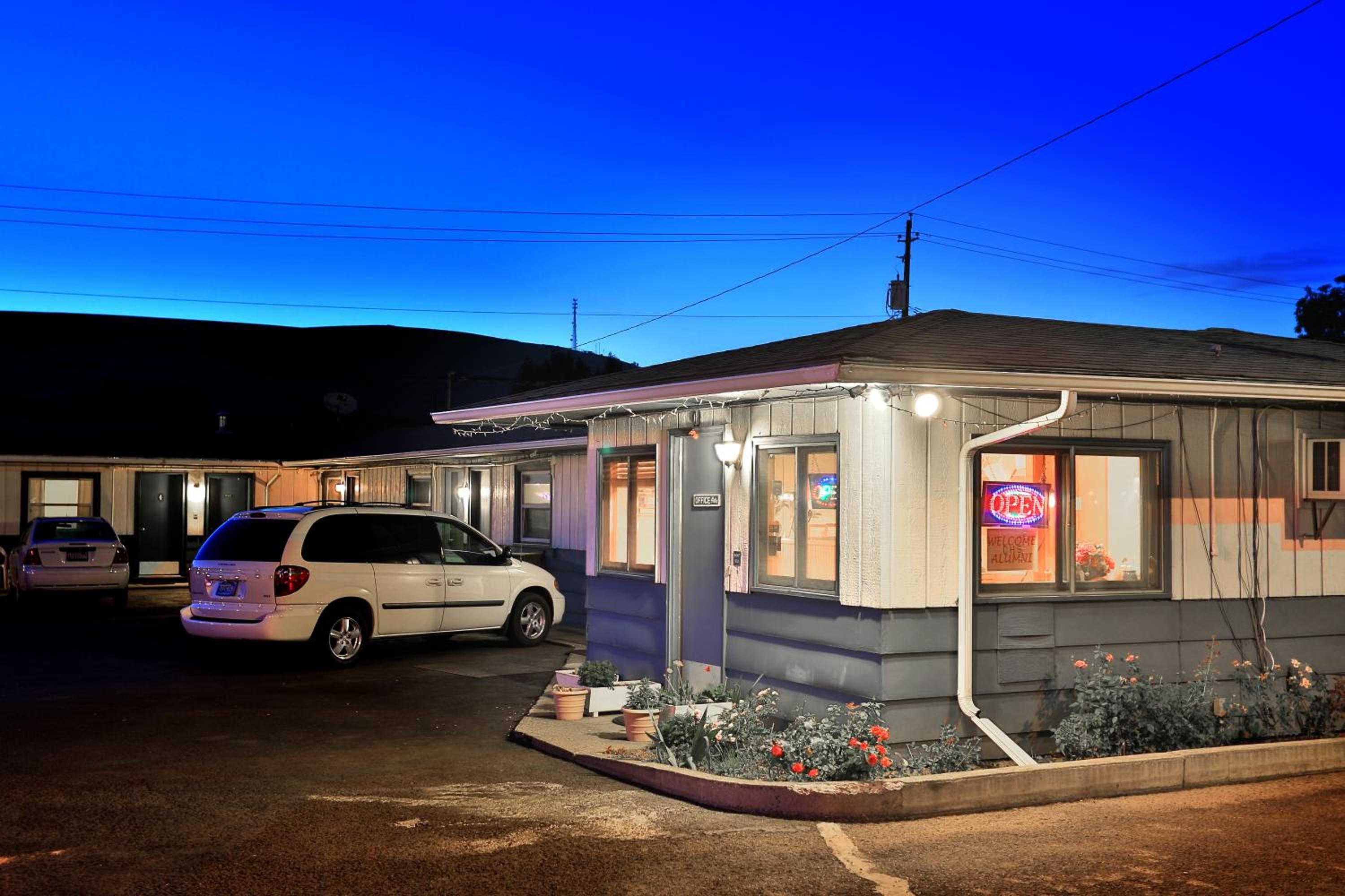A motel with a single-story structure, a parking area, and a small garden with potted plants.